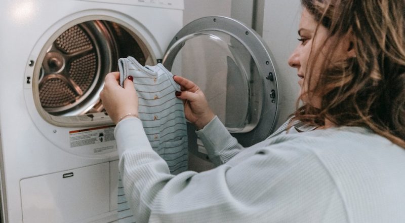 Mulher coloca roupa na máquina de lavar